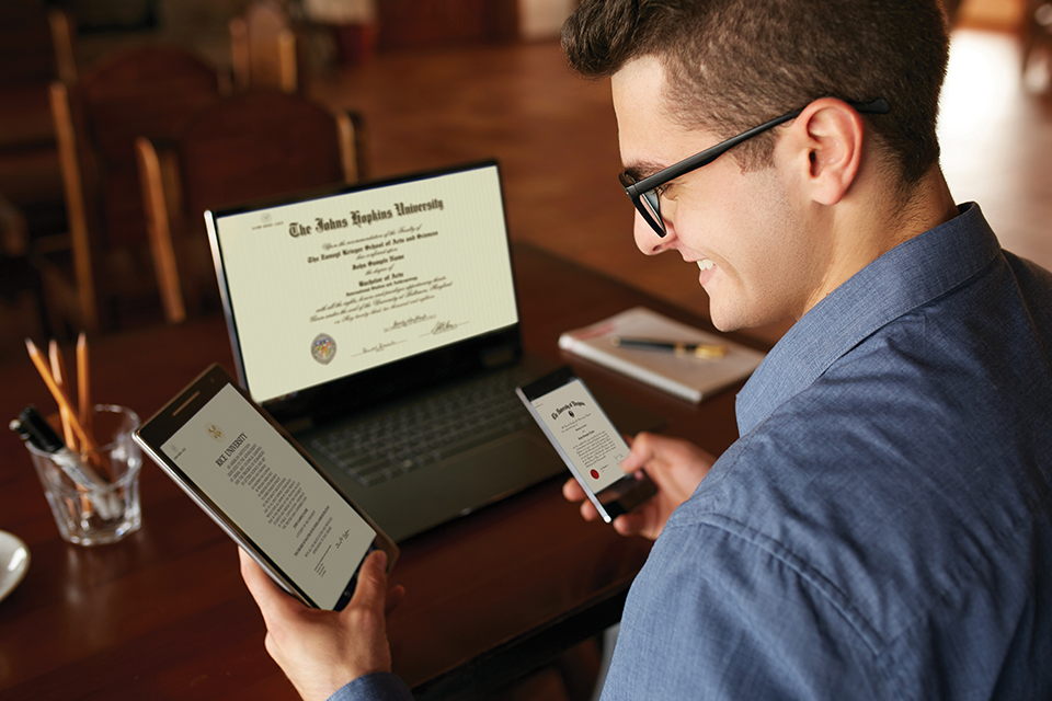 Guy holding tablet and phone, in front of laptop, with CeDiplomas on screens