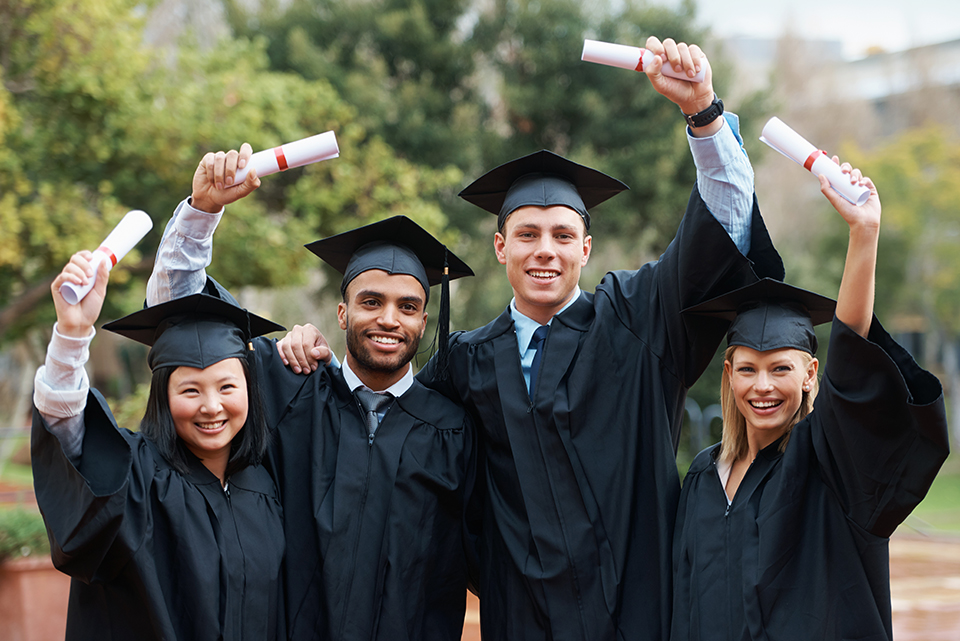 Four graduates together holding up their diplomas